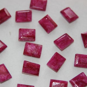 Könnte beinhalten: Eine Sammlung von 15 rechteckigen, facettierten, rosafarbenen Rubin-Edelsteinen. Die Steine sind alle ungefähr gleich groß und geformt.