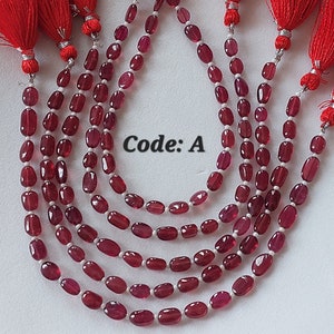 Puede incluir: Una hebra de cuentas de piedras preciosas rojas con un borla en cada extremo. Las cuentas son de forma ovalada y tienen un acabado brillante. La hebra está etiquetada como "Código: A".