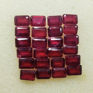 Op de afbeelding: Een verzameling van 20 rechthoekige, gefacetteerde, donkerrode edelstenen. De edelstenen zijn gerangschikt in vier rijen van vijf.