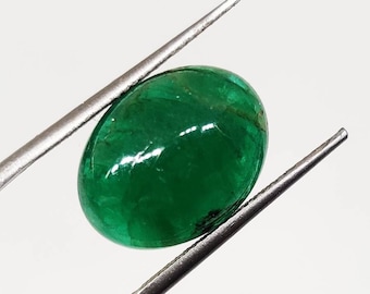 Pode incluir: Uma gema de esmeralda oval de cor verde vibrante mantida por pinças. A esmeralda tem uma superfície lisa e polida e uma cor verde profunda e rica.