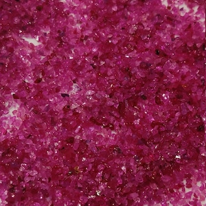 以下が含まれることがあります： ピンクのルビーの小さな宝石の山をクローズアップで見た様子。ルビーは不規則な形をしていて、さまざまなサイズがあります。
