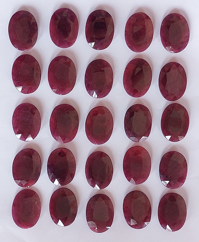 Puede incluir: Veinticinco piedras preciosas ovaladas de color rojo. Las piedras preciosas est&aacute;n dispuestas en cinco filas de cinco, sobre una superficie blanca.