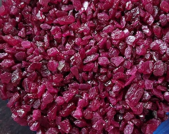 May include: A clear glass bowl filled with small, irregularly shaped, deep red gemstones. The gemstones are densely packed, creating a textured surface. The bowl sits on a dark surface.