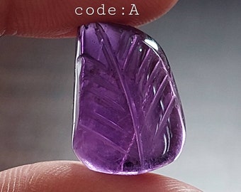 May include: A carved amethyst gemstone in the shape of a leaf. The gemstone is a deep purple colour and has a smooth, polished finish. The text "code: A" is visible in the image.