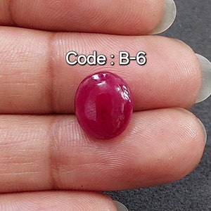 Op de afbeelding: Een ovale edelsteen in dieprode kleur met een glad, gepolijst oppervlak. De edelsteen wordt in een hand gehouden, en de tekst "Code: B-6" is zichtbaar boven de edelsteen.