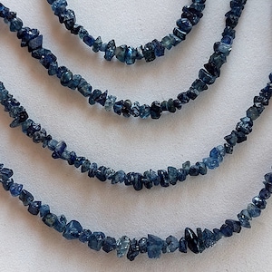 Könnte beinhalten: Vier Stränge blauer Saphir-Edelsteinkugeln, jeder Strang ist unterschiedlich lang, die Kugeln sind unregelmäßig in Form und Größe, die Kugeln sind auf einem durchsichtigen Faden aufgefädelt.