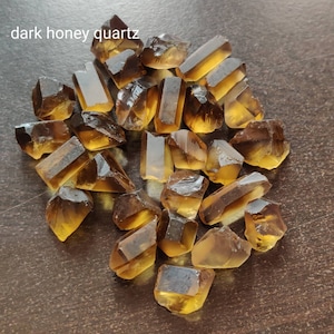 May include: A collection of dark honey quartz crystals, also known as smoky citrine, in various sizes and shapes. The crystals are a deep amber color with a translucent quality.
