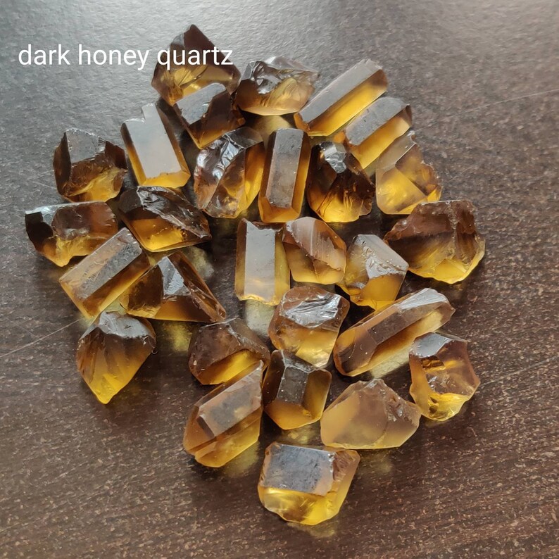 May include: A collection of dark honey quartz crystals, also known as smoky citrine, in various sizes and shapes. The crystals are a deep amber color with a translucent quality.