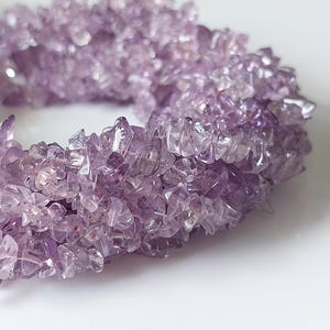 May include: A bracelet composed of numerous small, irregular, tumbled amethyst stone chips. The stones exhibit varying shades of translucent light to deep purple, creating a textured, multi-layered appearance throughout the circular band structure.