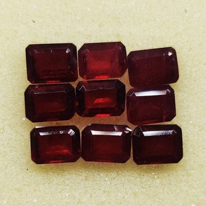 Puede incluir: Nueve piedras preciosas rectangulares rojas, probablemente granates, dispuestas en tres filas sobre un fondo blanco.