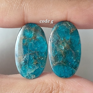 Op de afbeelding: Twee ovale turquoise edelstenen met een marmerpatroon en gouden vlekken. De stenen zijn ongeveer 2,5 cm lang.