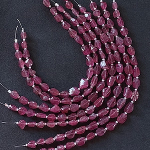 May include: A strand of pink tourmaline beads, with a rough, faceted, and irregular shape. The beads are strung on silver wire.