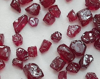 Peut inclure: Une collection de pierres précieuses de rubis rouges en vrac de différentes tailles et formes. Les rubis sont dispersés sur une surface blanche.