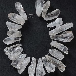 May include: A strand of clear quartz crystal points, arranged in a circle on a black background. The points are all roughly the same size and shape, and they have a natural, unpolished finish.
