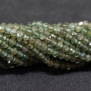 Könnte beinhalten: Eine Strähne aus facettierten grünen Edelsteinperlen. Die Perlen sind klein und rund, mit einer leicht unregelmäßigen Form. Sie haben eine durchscheinende Optik und eine hellgrüne Farbe.