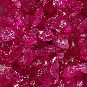 Könnte beinhalten: Nahaufnahme eines Haufens rosa, facettierter, kristallartiger Steine. Die Steine sind durchscheinend und haben einen leichten Schimmer.