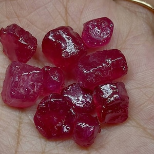 May include: A collection of eight faceted ruby gemstones, each with a deep red colour and a shiny, polished finish.