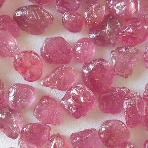 Könnte beinhalten: Eine Sammlung loser rosa Rubin-Edelsteine. Die Rubine sind in verschiedenen Größen und Formen, wobei einige einen polierteren Look haben als andere.