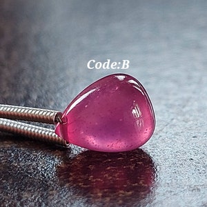 Può includere: Primo piano di un ciondolo a forma di lacrima di pietra preziosa rosa su una catena d'argento. Il ciondolo è liscio e lucido, con un leggero luccichio. Il testo "Codice: B" è visibile nell'immagine.