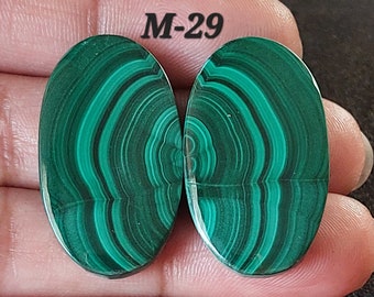 Pode incluir: Dois cabochões ovais de malaquita verde com um padrão de redemoinho. Os cabochões são etiquetados como "M-29".