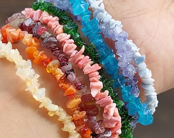 Puede incluir: Un conjunto de siete pulseras hechas con cuentas de piedras preciosas astilladas. Las pulseras están superpuestas en la muñeca de una persona y presentan una variedad de colores, incluyendo blanco, azul claro, azul, verde, rosa, rojo y naranja.