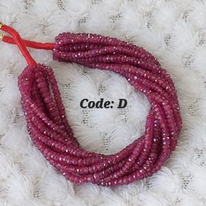 May include: Strands of faceted, deep pink beads are bundled together, tied with red cord. The beads are arranged in multiple rows, creating a full, textured appearance. The text "Code: D" is visible.