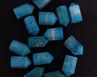 Könnte beinhalten: Eine Sammlung von zwölf blauen und grünen Edelstein-Spitzen, auch bekannt als Kristallspitzen, die auf einer schwarzen Oberfläche angeordnet sind. Die Spitzen sind alle ungefähr gleich groß und geformt und haben eine glatte, polierte Oberfläche.