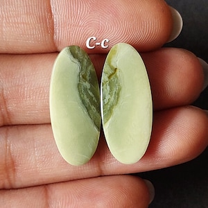 以下が含まれることがあります： 緑と白の楕円形のジェムストーンカボションが2つ。カボションは滑らかで磨かれています。カボションの上に「C-c」という文字が書かれています。