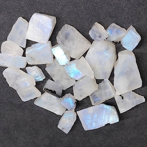 May include: A collection of white moonstone crystals with iridescent blue and green flashes. The crystals are various shapes and sizes, and some have a rough, natural texture.