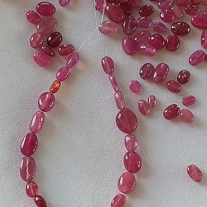 May include: A strand of pink oval-shaped beads strung on a silver thread. The beads are loose and ready to be made into a necklace or bracelet.