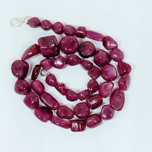 May include: A strand of deep red ruby gemstone beads, each bead is a different shape and size, the beads are strung on a silver chain.