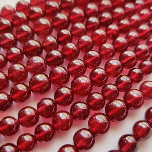 May include: A strand of deep red gemstone beads. The beads are round and smooth, with a glossy finish.