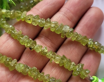 May include: A strand of green peridot gemstone beads, each bead is a rough, irregular shape. The beads are strung on a cord and have a tassel at the end.