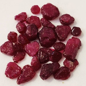 May include: A collection of loose, red ruby gemstones of various sizes and shapes. The rubies are rough and unpolished, with a deep red color.