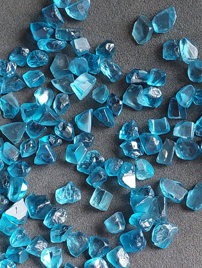 May include: A collection of loose, faceted, teal blue gemstones. The gemstones are various sizes and shapes, and have a shiny, polished finish.