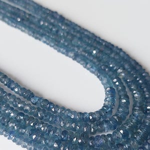 Puede incluir: Un hilo de cuentas de piedras preciosas azules, redondas y facetadas, dispuestas en un bucle de varias capas. Las cuentas muestran una calidad translúcida con tonos variables de azul profundo y claro, reflejando la luz en sus caras.