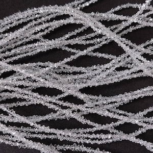Pode incluir: Uma corda de contas de cristal transparente e facetadas. As contas são pequenas e têm uma textura áspera e natural. As contas são enfiadas em um fio transparente e estão dispostas em um padrão solto e fluido.