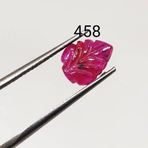 Op de afbeelding: Een gesneden robijn edelsteen in de vorm van een blad. De edelsteen is diep roze van kleur en wordt vastgehouden door een pincet. De afbeelding is gelabeld met "458".