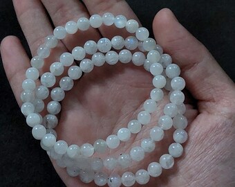 May include: A white moonstone beaded bracelet with iridescent shimmer. The bracelet is made of round beads and is layered in a triple strand design.