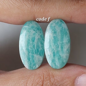 Peut inclure: Deux cabochons ovales en amazonite verte et blanche, avec une surface lisse et polie. Les pierres mesurent environ 2,5 cm de long.