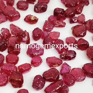 May include: A collection of loose, red ruby gemstones. The rubies are various shapes and sizes, with some having a more polished finish than others.
