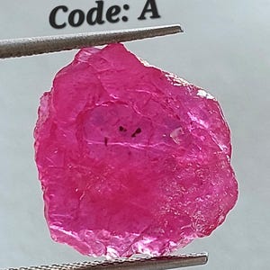 May include: A pink, rough, uncut ruby gemstone with a code 'A' label.