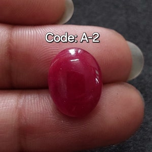 Op de afbeelding: Een close-up van een dieprode ovale edelsteen. De edelsteen is glad en glanzend, met een lichte reflectie van licht. De tekst "Code: A-2" is zichtbaar in de afbeelding.