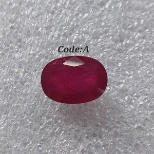 Peut inclure: Une pierre précieuse ovale de couleur rouge foncé avec une taille facetée. La pierre précieuse est sur un fond blanc avec le texte "Code: A" au-dessus.