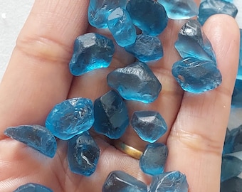 Peut inclure: Une collection de pierres précieuses d'apatite bleue, certaines avec une taille facetée, d'autres avec une finition brute et naturelle. Les pierres sont de tailles et de formes variées et sont présentées sur une main.