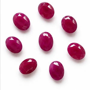 May include: Seven oval-shaped, faceted rubies arranged in a circular pattern. Each gemstone displays a deep, saturated magenta-red colour with a polished surface that reflects light across its multiple cut facets, creating a brilliant appearance.