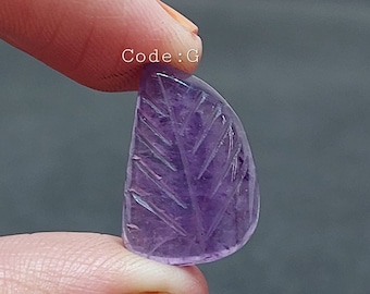 May include: A carved amethyst gemstone in the shape of a leaf. The gemstone is a light purple colour and has a smooth, polished finish.
