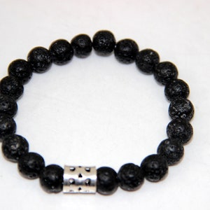 Può includere: Bracciale con perline in pietra lavica nera con un accento in metallo argentato. Il bracciale presenta perline rotonde e porose infilate insieme, creando un aspetto strutturato. L'accento argentato ha un motivo geometrico.