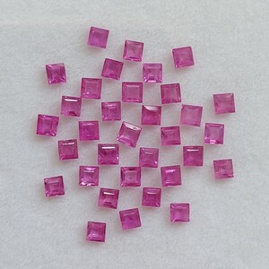 Puede incluir: Una colección de piedras preciosas cuadradas de color rosa, esparcidas sobre una superficie blanca.