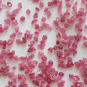 以下が含まれることがあります： 白い表面に散らばった、小さく、ざらざらしたピンクのルビーの結晶のコレクション。結晶はさまざまな形とサイズで、いくつかは他のものよりも不透明に見えます。